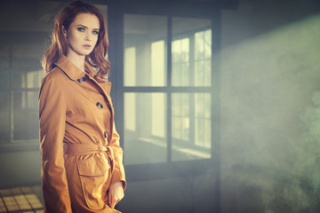 Beautiful fashionable girl stands near the window wall . Smoke cinema photo
