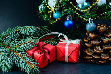 Pine cone and gifts wrapped in a red paper with white ribbon under decorated Christmas tree. Concept of Merry Christmas and New Year