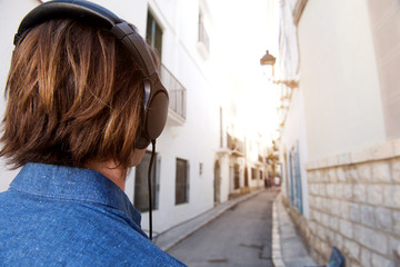 Rear of man with long hair looking at city street with headphones