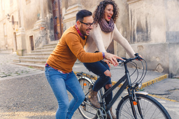 Fototapeta premium Happy young couple having fun riding a bicycle on sunny autumn day in the city.