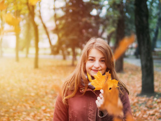 young woman walking in autumn Park on a Sunny day. Beautiful nature in autumn season. Happy smiling woman with bouquet of autumn maple leaves