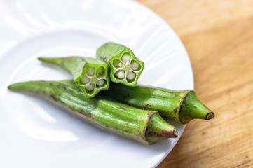Fresh okra in white dish on wooden table.