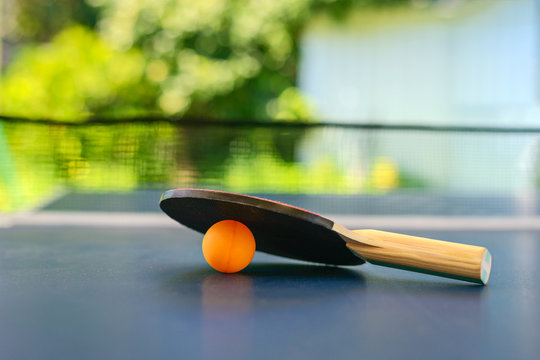 Table tennis table with racket and orange ball on backyard
