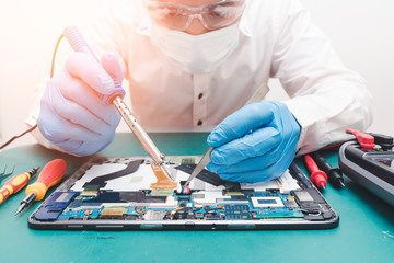The abstract image of the asian technician repairing a tablet by soldering iron in the lab. the...
