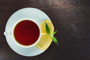 White cup of tea with cinnamon sticks, lemon, mint leaves and tea strainer on wooden rustic table.