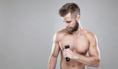 Handsome bearded man with a trimmer shaving off body hair