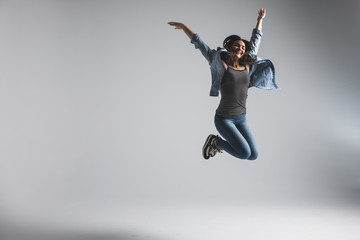 Fototapeta premium Playful young woman wearing casual jumping over grey background. Look at camera and screaming.