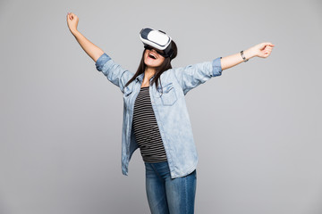Attractive and happy woman using virtual reality goggles celebrate victory gesture on grey background. VR headset.