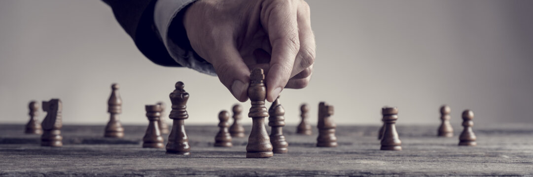 Wide cropped image of a human hand wearing business suit moving dark King chess piece