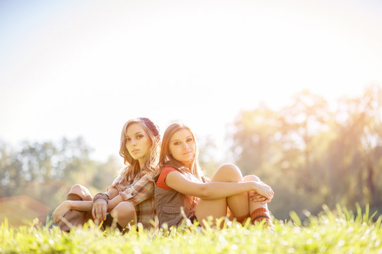 two young females sitting back to back on grass