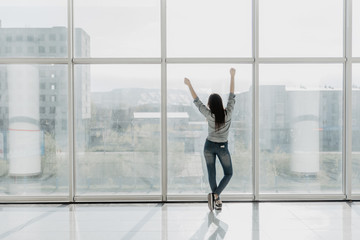 Fototapeta na wymiar Confident woman spreading hands standing at office window, enjoying big city, successful entrepreneur celebrating business success with arms open wide, feeling powerful inspired, rear view