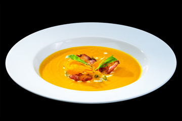 Delicious and appetizing pumpkin cream soup with chips in a white plate isolated on black background. Autumn menu in an Italian restaurant. Photo for menu design