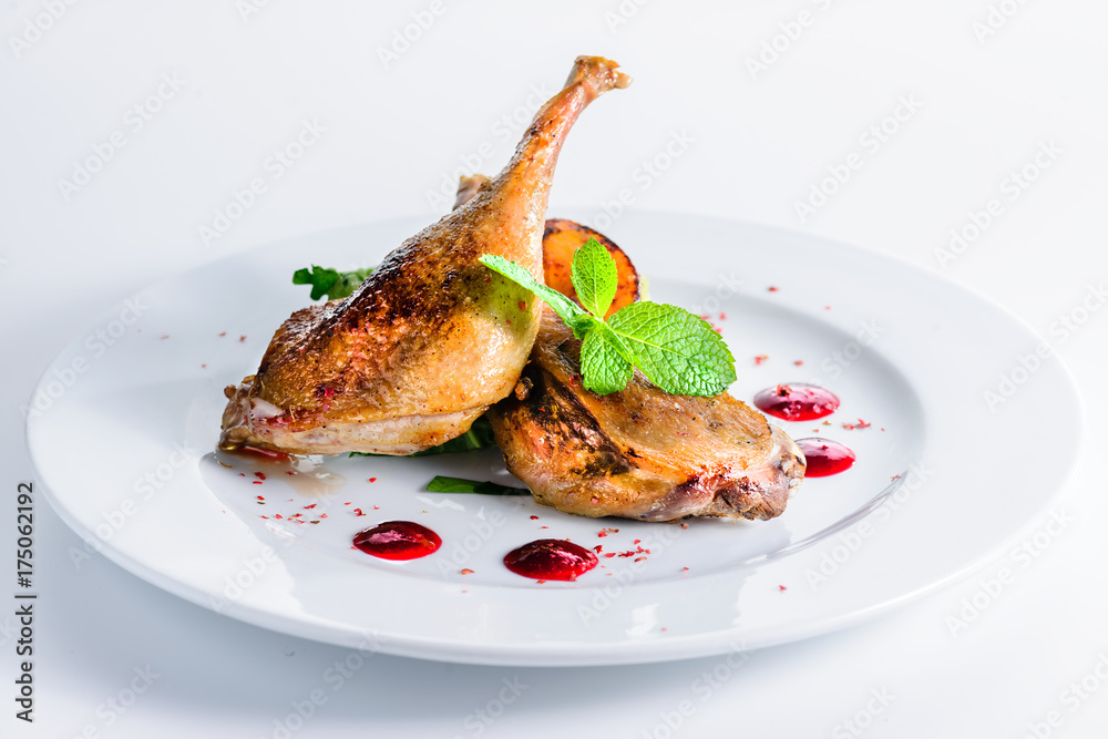 Sticker juicy delicious cooked duck legs served with herbs and sauce in a white plate over white background.