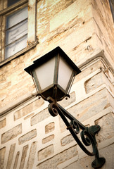 Street lamp of vintage design lighted on the stone wall in the afternoon.Syros island.Greece