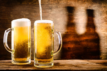 Glass of light beer on a wooden background with shadow of two bottles of beer