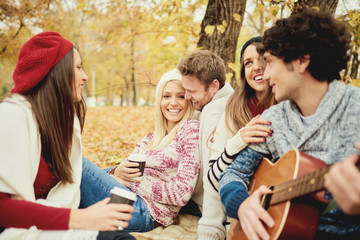     Friends having a good time in park at autumn/ singing and playing guitar 