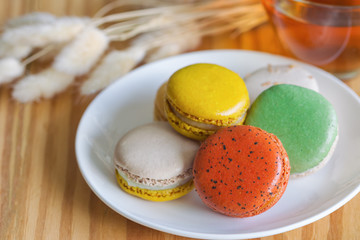 Colorful French macaron or Italian macaron on white plate. Homemade delicious macaron and tea on wood table with copy space for background or wallpaper. Macaron is popular dessert for served with tea.