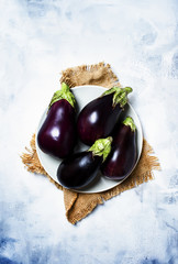 Fresh purple eggplants on plate, stone background, top view