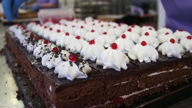 Sprinkle with chocolate cakes. White cream on dark cakes. Red berries on white cream. Rectangular cake. Production of sweet dessert. FullHD. Soundless.