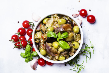 Stewed aubergines with bell pepper, tomato, olives and herbs, white background, top view