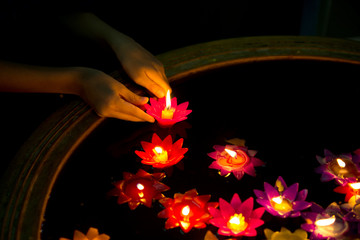 Hands of Buddhist floating colorful Candle floating on water for pray buddha at night.