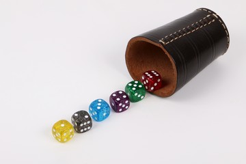 Würfelbecher mit einer Reihe von bunten Würfeln liegt auf dem Tisch