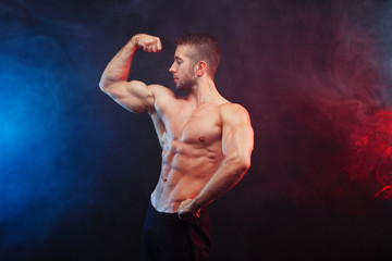 Obraz premium Muscled man model posing on dramatic smoky background. Sports, bodybuilding, healthy lifestyle concept