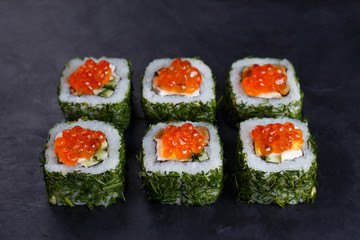Japanese food, sushi restaurant. Delicious sushi rolls topped with caviar in chopped dill served on black slate with free space for text design