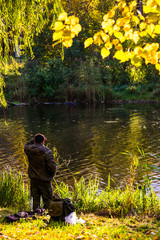 The fisherman stands on the shore of the lake in autumn