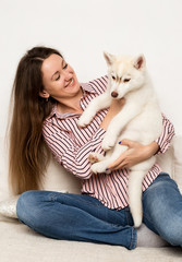 Happy beautiful woman hugging puppy husky. girl sitting on a sofa and puppy licks her