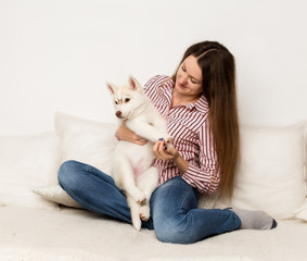 Obraz na płótnie Canvas Happy beautiful woman hugging puppy husky. girl sitting on a sofa with a dog