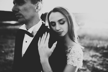 Happy newlywed couple posing and smiling in wedding dress and suit outdoor, black and white