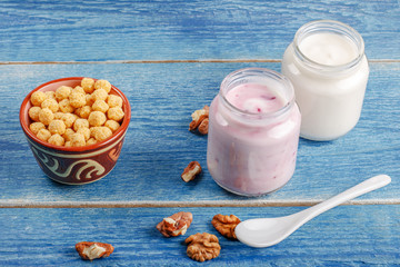 Healthy breakfast ingredients.Homemade yogurt in glass jars, ceramic bowl with oat flakes, walnuts, grapes on light blue background, copy space