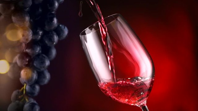 Wine. Red wine pouring in wine glass over dark background. Slow motion. 4K UHD video 3840x2160
