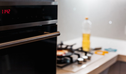 A beautiful kitchen with an oven and an electronic clock on it and a glass hob with cooking...