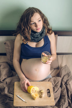 Pregnant woman lying in bed sick with colds and flu. Woman treated with lemon ginger tea and honey.