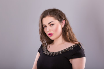 Portrait of a plus size female model posing in black dress over grey background.