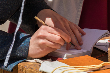 Close up of hands of scribe practicing traditional illumination writing calligraphy with feather quill and ink
