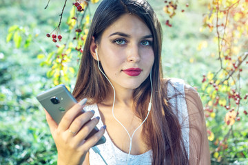 Woman listening to music in your phone wearing headphones on a Sunny day. Concept of audiobooks and student education