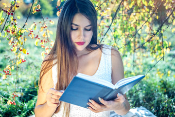 Obraz premium Woman reading an interesting book sitting in a Park on a green lawn on a Sunny summer day. Concept of student education