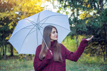 Happy young woman walking in a Sunny Park with a white umbrella in the rain. Concept of seasons and autumn mood