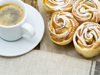 Cup of coffee and homemade pastries of flaky unleavened dough with apples on parchment paper