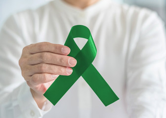 Liver Cancer and Hepatitis B disease awareness concept symbolic with emerald green or jade color ribbon in person's hand