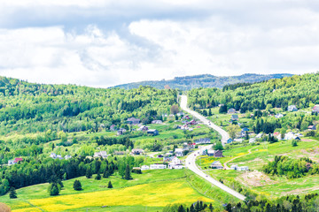 Les Eboulements, Charlevoix, Quebec, Canada cityscape or skyline with main highway steep curvy road going vertically up, patch farm green dandelion field, scattered village houses