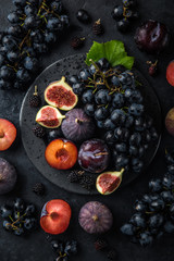 fresh dark fruits (grapes, figs, plum and blackberry) on black plate, concrete background