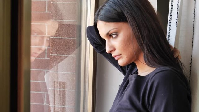 Close up of Face of a Pensive Pretty Depressed Young Woman, Looking Down by a Window, Worried or Sad.