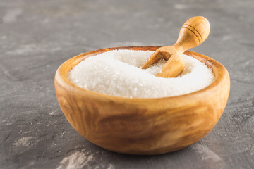 White sugar sugar in a wooden plate with a dustpan on a dark background.