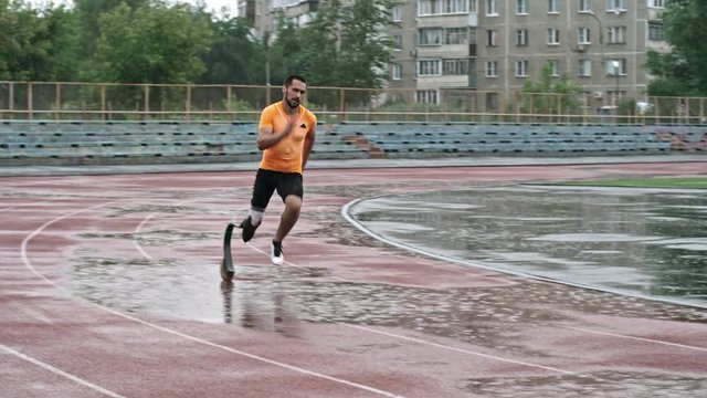 Amputee athlete with prosthetic leg running in the rain on stadium track