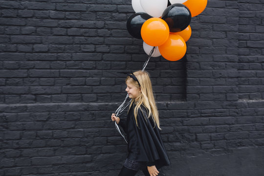 Blonde Girl in a Witch Halloween Costume Holding Balloons