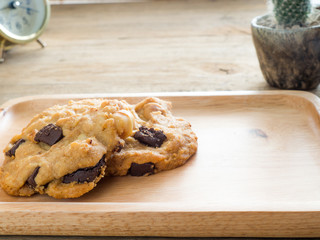 Cookies with chocolate and macadamia nuts. Placed on a wooden plate.The back is the old clock and cactus.Coffee brake concept.